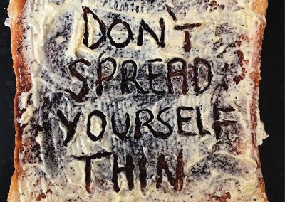 A photographic poster of a heavily buttered slice of toast with ‘Don’t spread yourself thin’ scraped out of the butter.